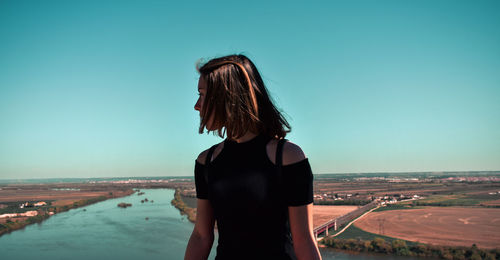 Young woman looking at river against clear blue sky