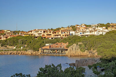 View of townscape by river against clear blue sky