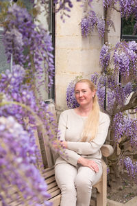 Beautiful middle-aged woman sits on a bench in the thickets of blooming wisteria