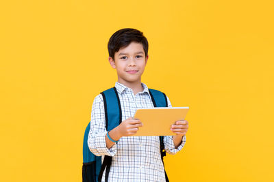 Full length of boy holding mobile phone against yellow background