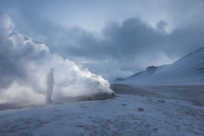 Man standing by fumaroles emitting steam on snow covered field