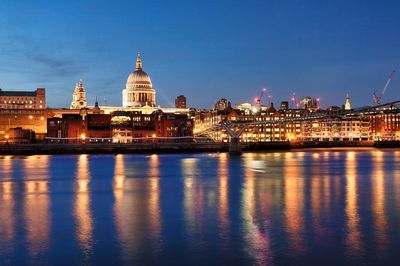 Millennium bridge over thames river by illuminated st paul cathedral against sky at dusk