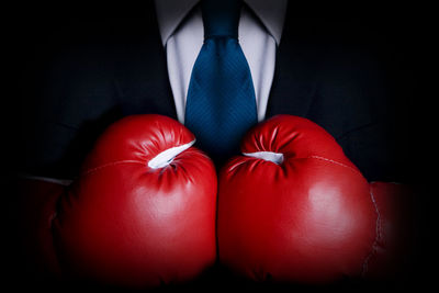 Midsection of businessman wearing boxing gloves against black background