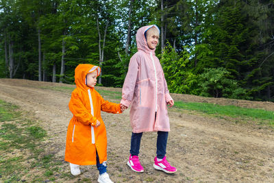 Siblings wearing raincoat while walking on pathway in forest