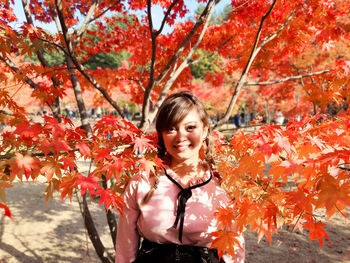 Portrait of young woman standing by tree during autumn