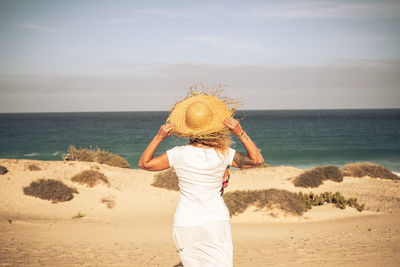 Rear view of woman wearing hat while looking at seascape