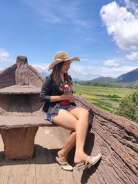 Woman sitting on wood against sky