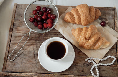 Tasty breakfast with fresh croissant, coffee, cherries on a wooden tray. breakfast pearl necklace