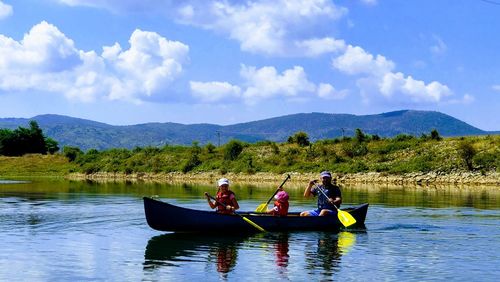 People sitting on rowboat in lake against sky