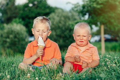 Toddler crying while brother eating ice cream on grass