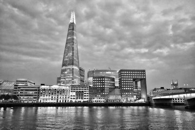 Low angle view of illuminated modern buildings by river against cloudy sky