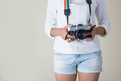 Midsection of woman with camera standing against white background