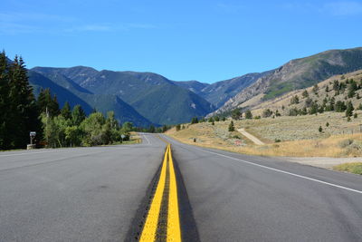 Empty road along mountains against clear blue sky