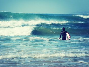 Rear view of surfer carrying surfboard in sea against sky