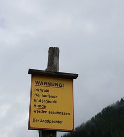 Low angle view of warning sign against sky