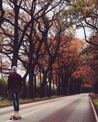 Rear view of man walking on road along trees