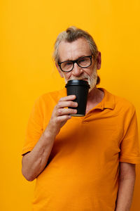 Portrait of senior man drinking coffee against yellow background