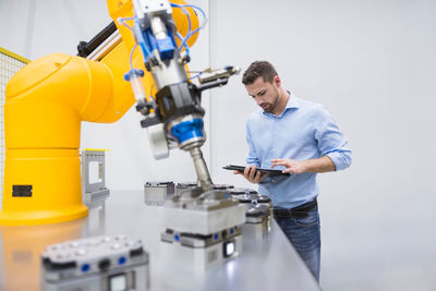 Engineer using tablet pc near robotic arm in factory