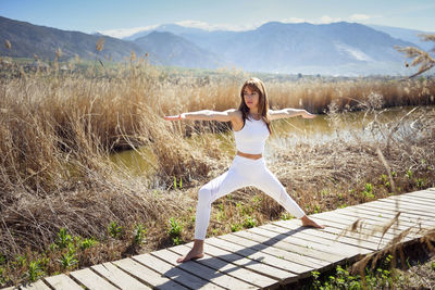 Full length of woman doing yoga on boardwalk against plants