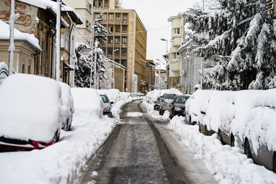 Snow covered road amidst buildings in city