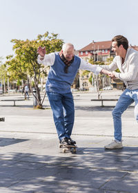 Adult grandson assisting senior man on skateboard