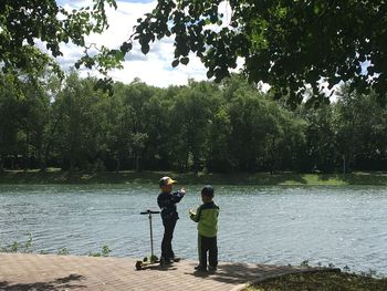 Rear view of people enjoying in lake against trees