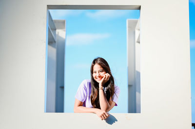 Portrait of smiling young woman standing against white wall