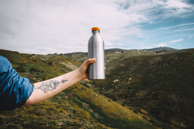 Cropped image of hand holding bottle against mountains
