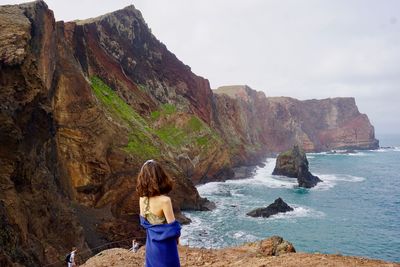 Rear view of woman on rock by sea against sky