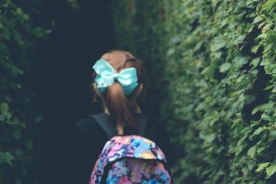 Rear view of girl with backpack walking by trees in forest