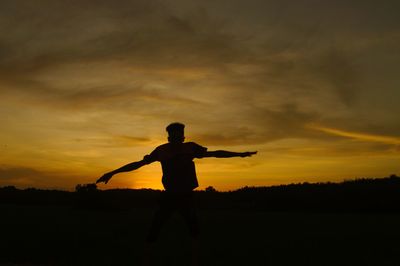 Silhouette man standing on field against sky during sunset