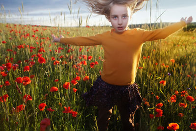 Portrait of cute girl standing by poppy field against sky