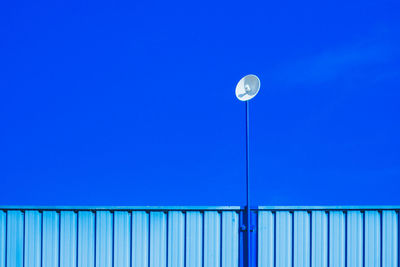 Low angle view of satellite dish on corrugated iron against blue sky