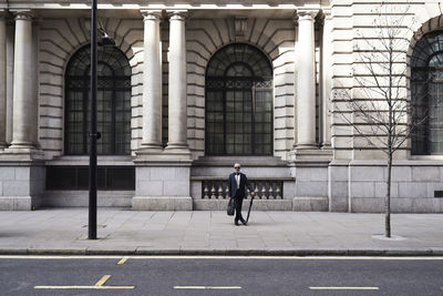 Uk, london, stylish senior businessman with briefcase and umbrella standing on pavement