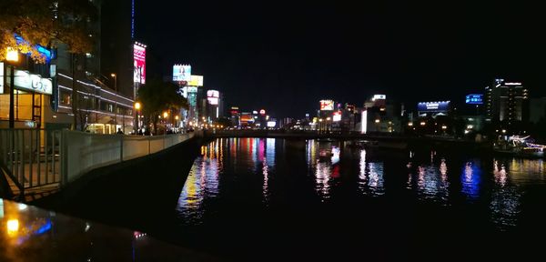 Illuminated buildings by river against sky at night