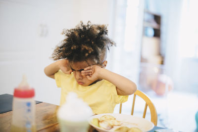 Boy rubbing eyes while sitting at table