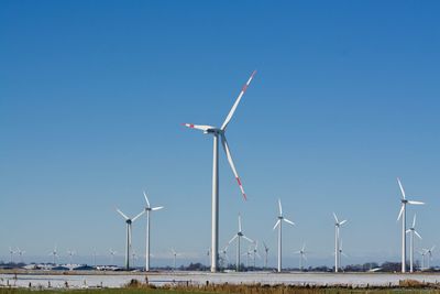 Wind turbines on field against clear blue sky