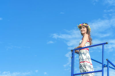 Low angle view of woman wearing flowers while standing by railing against sky