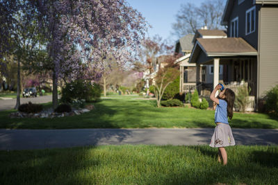 Side view of girl looking through binoculars while standing on grassy field at yard