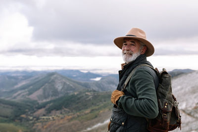 Side view of elderly male traveler with backpack standing in highlands in winter and admiring scenic landscape in caceres