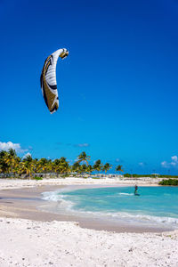 Man kiteboarding in sea against blue sky