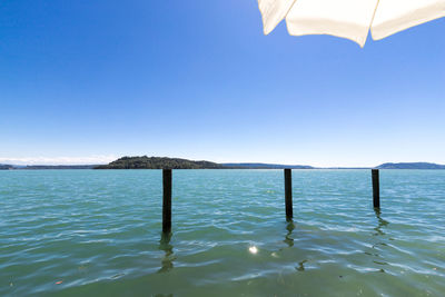 Wooden posts in sea against clear blue sky