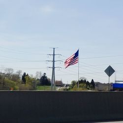 Flag by electricity pylon against sky