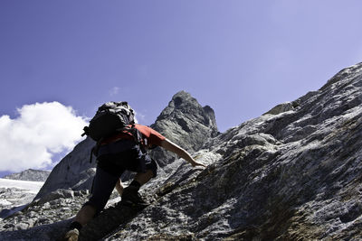 Low angle view of man climbing mountain against sky during sunny day