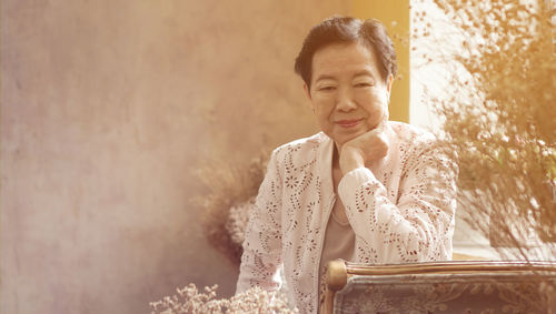 Portrait of smiling senior woman sitting against wall