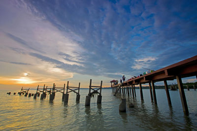 Wooden posts in sea against sky at sunset