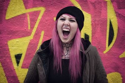Portrait of hipster woman screaming while standing against wall