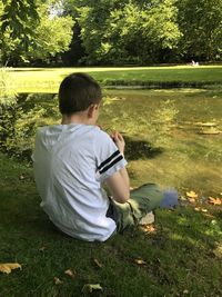 Rear view of boy sitting by lake at park