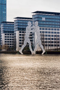 Statue by modern buildings in city against sky