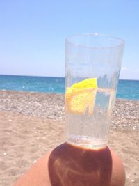 Close-up of hand holding drink at beach against clear sky